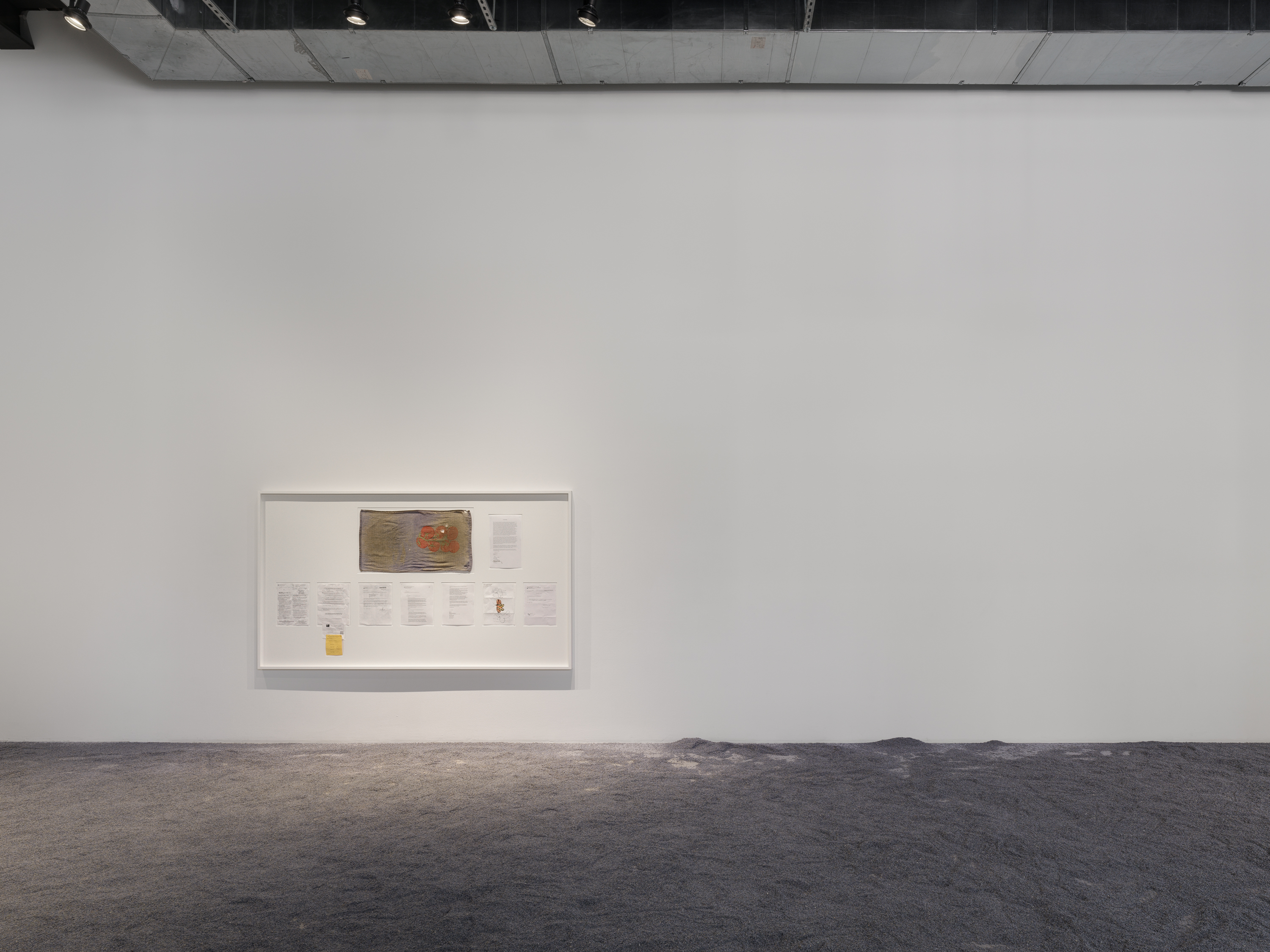 White-framed display of exhibition documents mounted on a white wall.